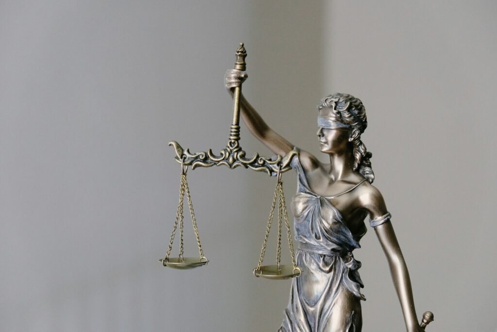 Bronze statue of Lady Justice, blindfolded, holding a balance scale with equal pans. Ornate details on the scale and statue's drapery are visible. Justice is symbolized by the balanced scale.
