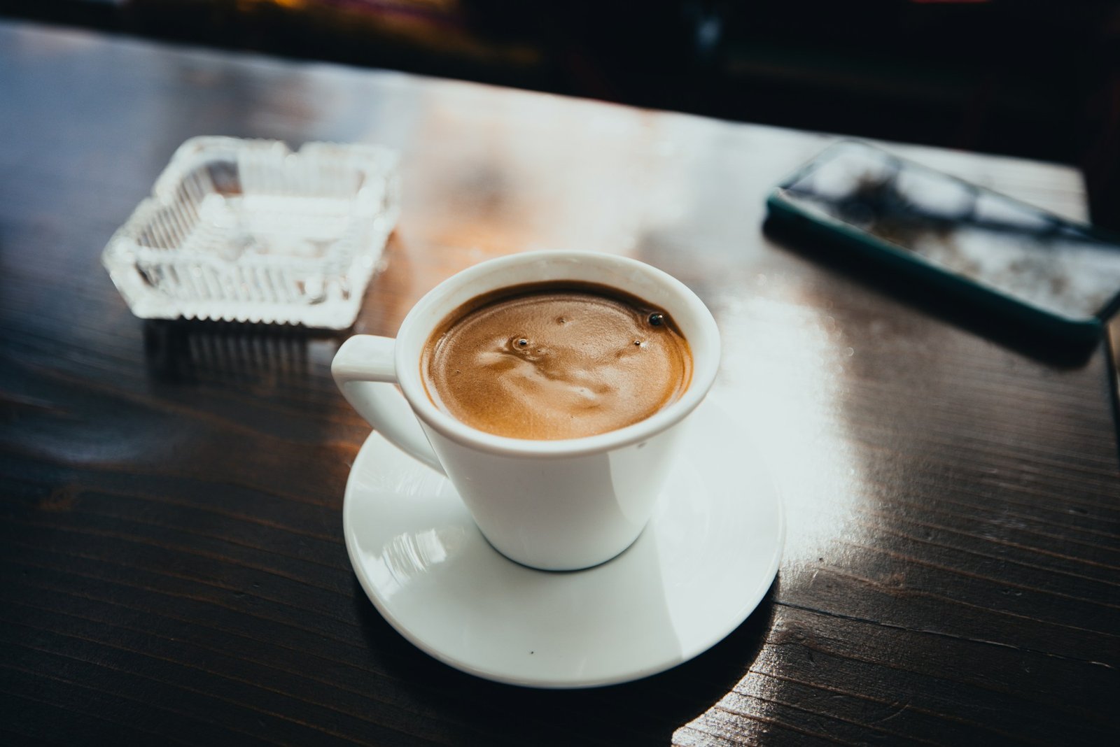 White coffee cup with espresso on wooden table next to smartphone and decorative tray
