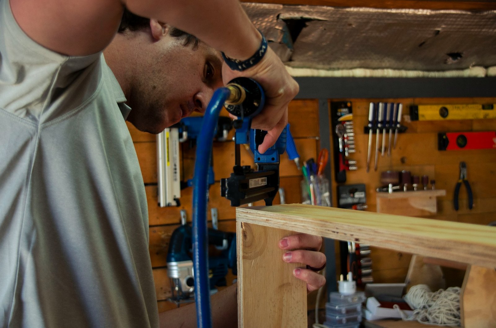 Person using blue woodworking clamp on wooden board in workshop with tools visible on pegboard wall