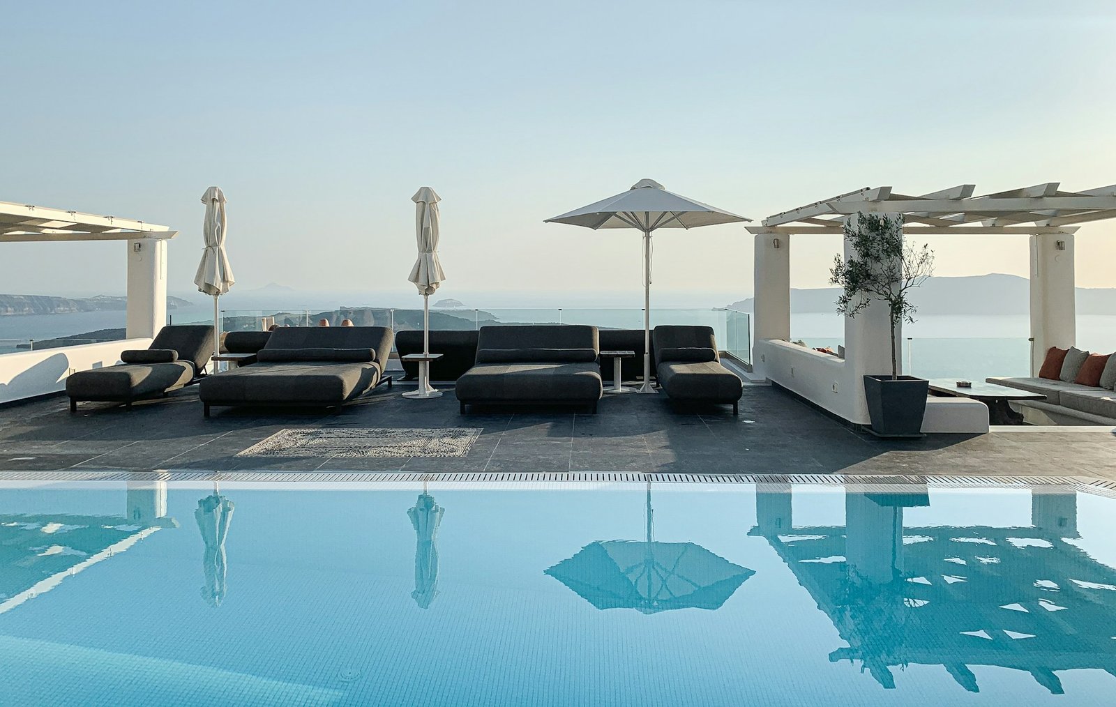 Luxury poolside area with black lounge chairs, umbrellas, and infinity pool overlooking ocean at sunset
